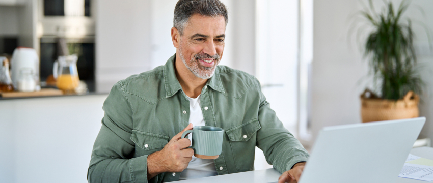 A man at a table uses a laptop for forex trading analysis, with a cup of coffee beside him.