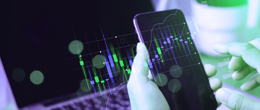 A person holding a smartphone showcases mobile analysis of a digital stock chart, while a laptop in the background displays green and white candlestick patterns, highlighting the account-open trading process.
